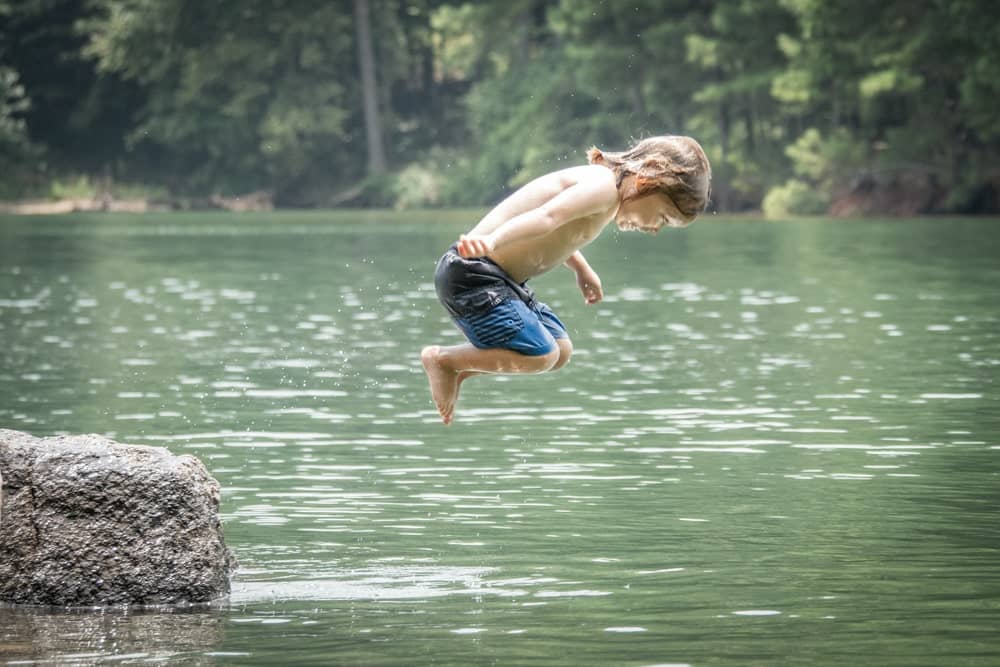 boy jumping from rock into lake