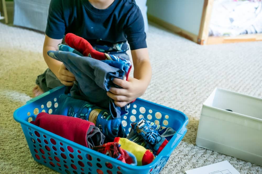 Child putting folder clothes in a blue bin