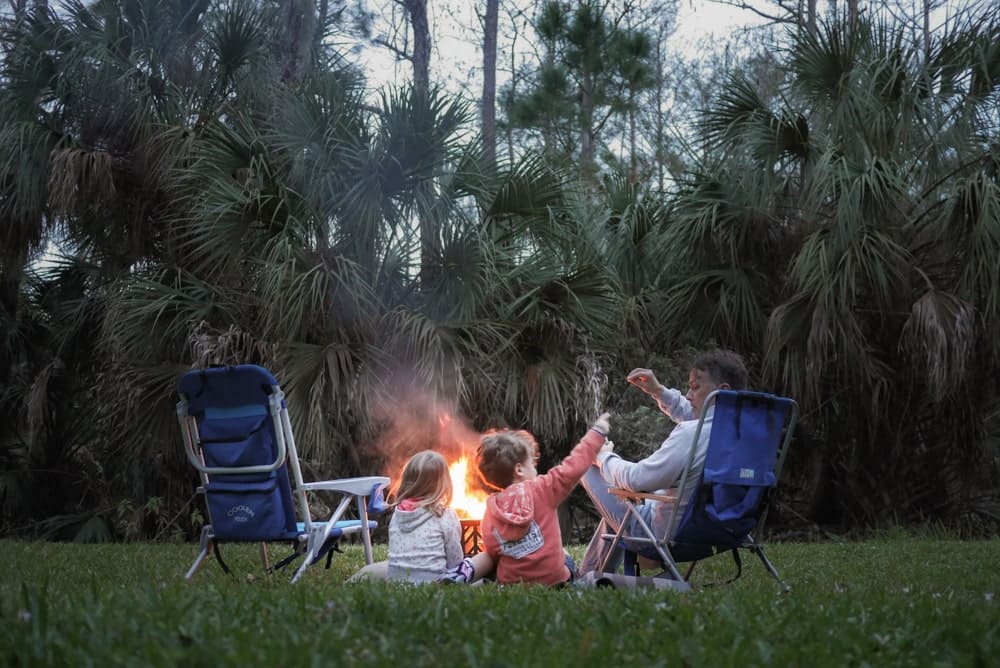 boy, girl, and man sitting on chairs in front of campfire