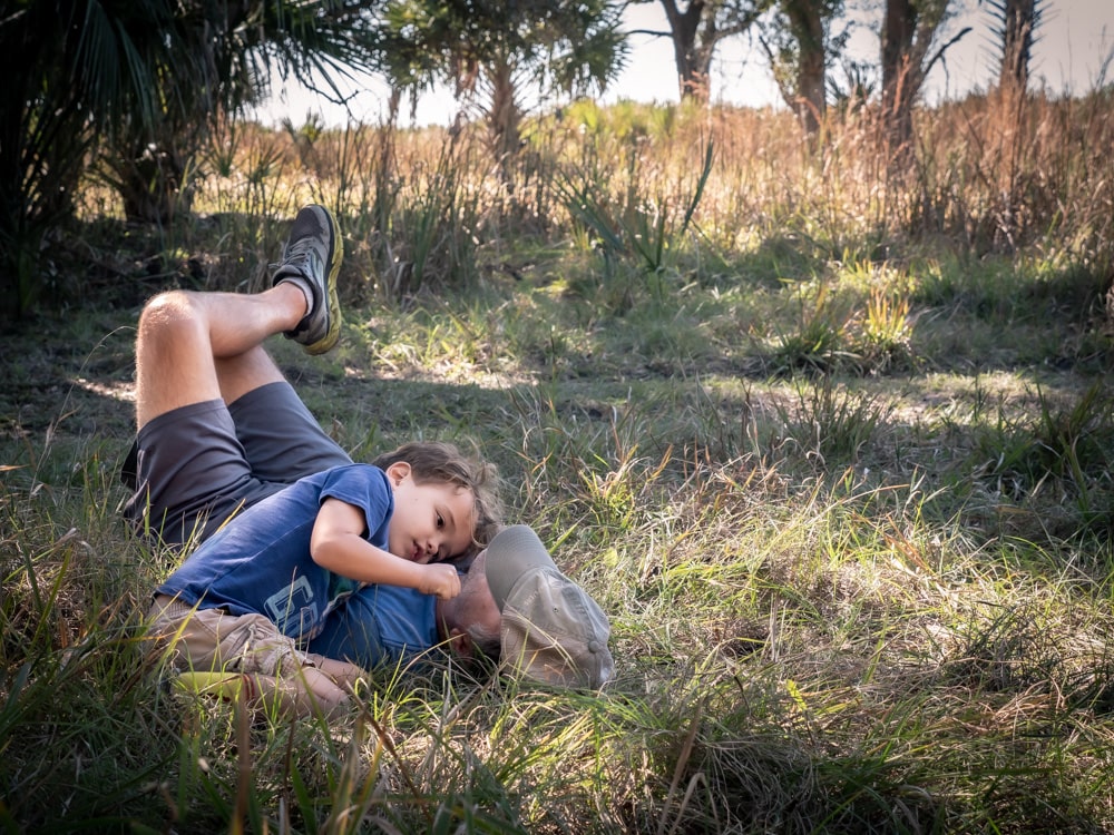 man laying on grass with boy resting his head on man