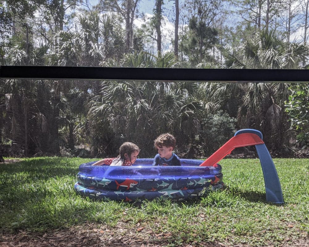 Boy and girl playing in inflatable pool in backyard