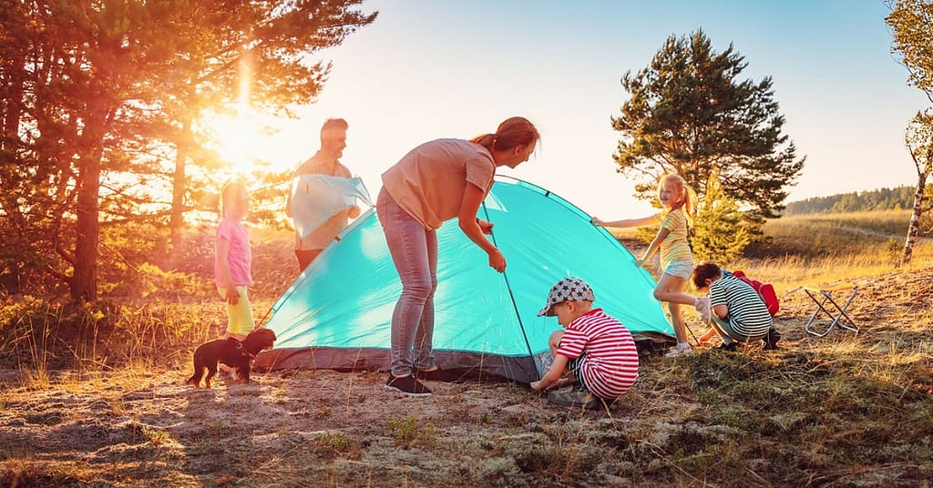 Family with three small children setting up a small blue camping tent