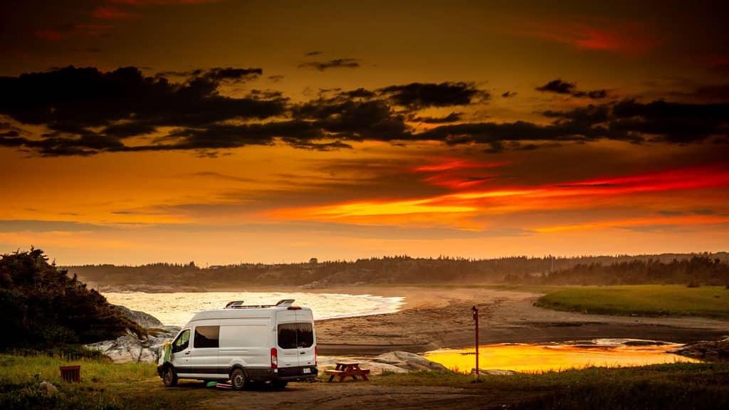 class B van dry camping by lake with sunset sky in background