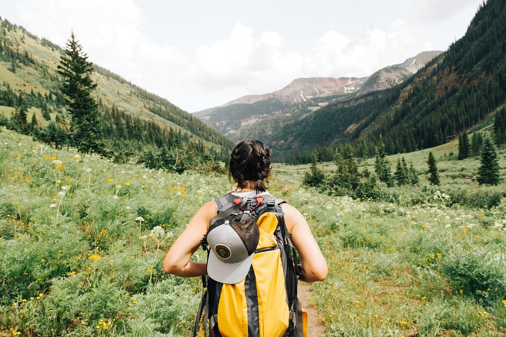 woman outdoors carrying orange backpack hiking towards a mountain