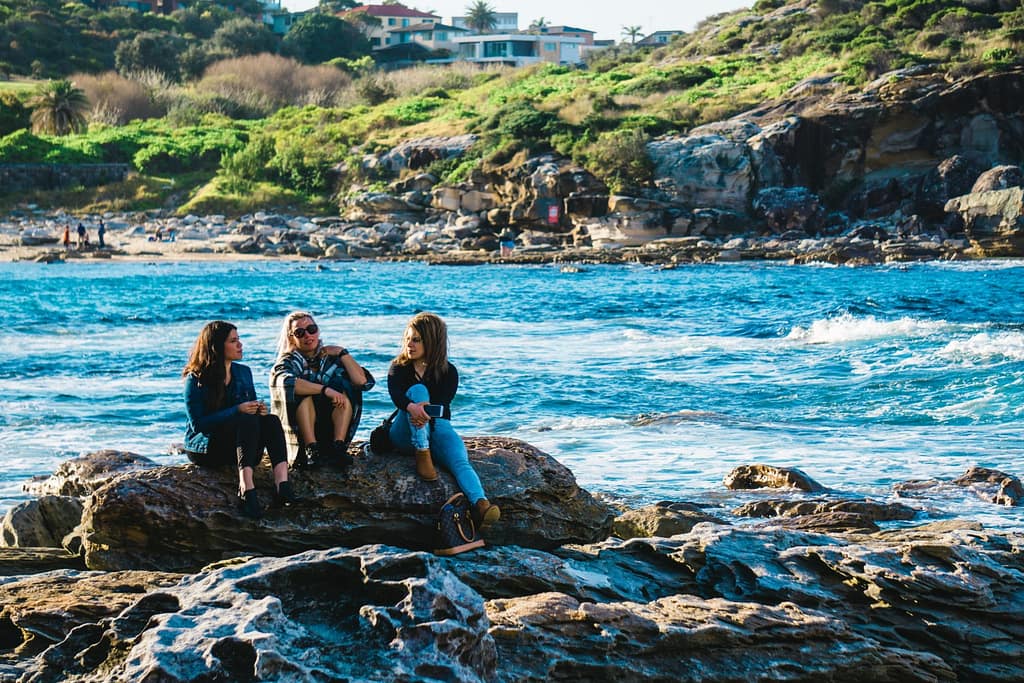 three women sitting on rocks by the ocean having a conversation