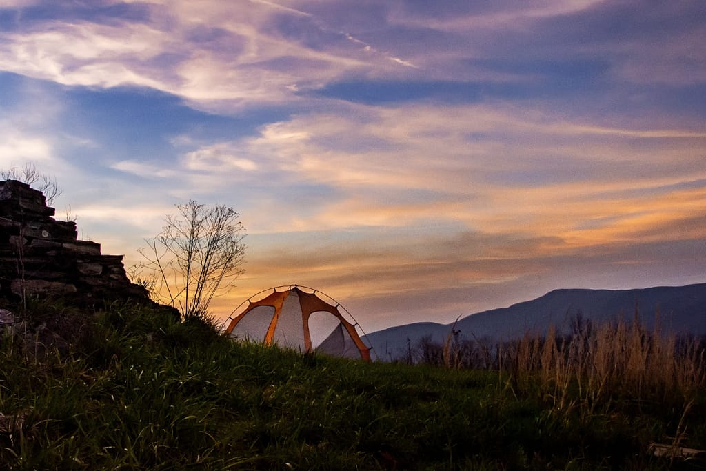 small camping tent with blue and orange sunrise sky in the background