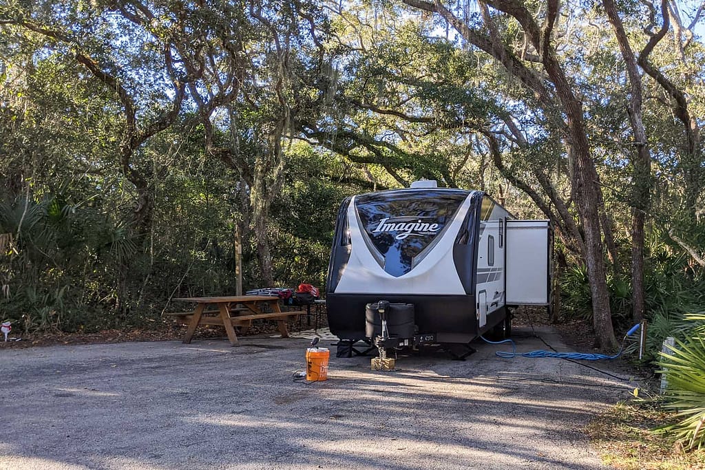 Travel trailer in a camp site under shady trees and a picnic table by it in Anastasia State Park