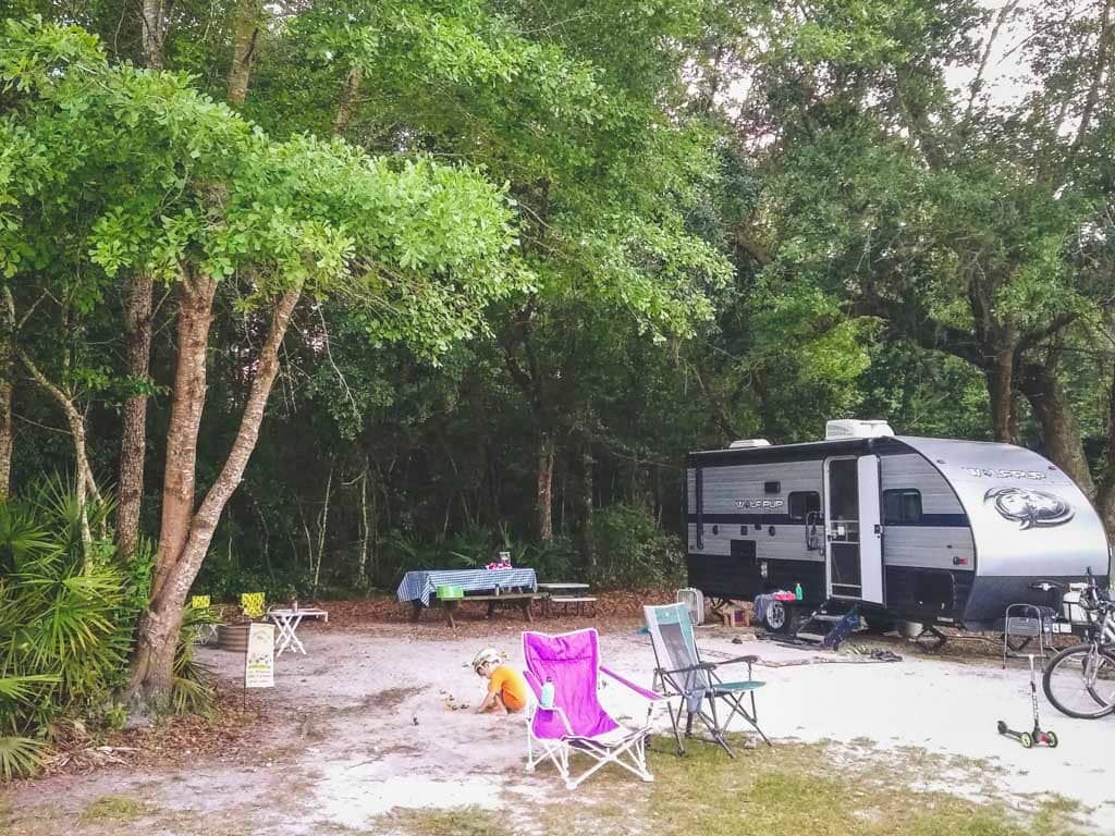 Travel trailer on campsite, under oak trees, kids playing in front. Site 7 at Hart Springs Park.
