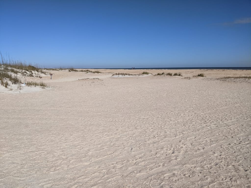 Large expanse of sand with dunes and blue sky in the background