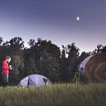 Man standing next to tent in open field at night