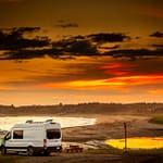 class B van dry camping by lake with sunset sky in background