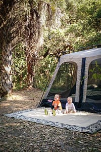toddler and baby sitting on rug in front of camping tent