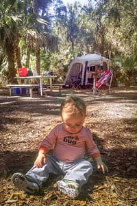 baby sitting on ground in front of camping tent