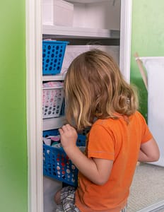 Little girl in orange shirt looking for clothes in closet