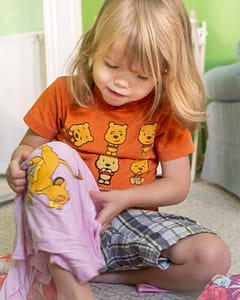 Little girl in orange shirt looking at a shirt on her lap
