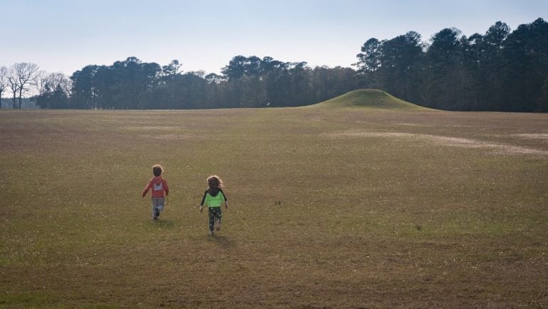 Two little kids running on open grass field at Kolomoki Mounds State Park