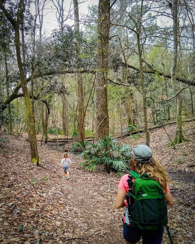 woman carrying backpack on hiking trail with two small kids in front